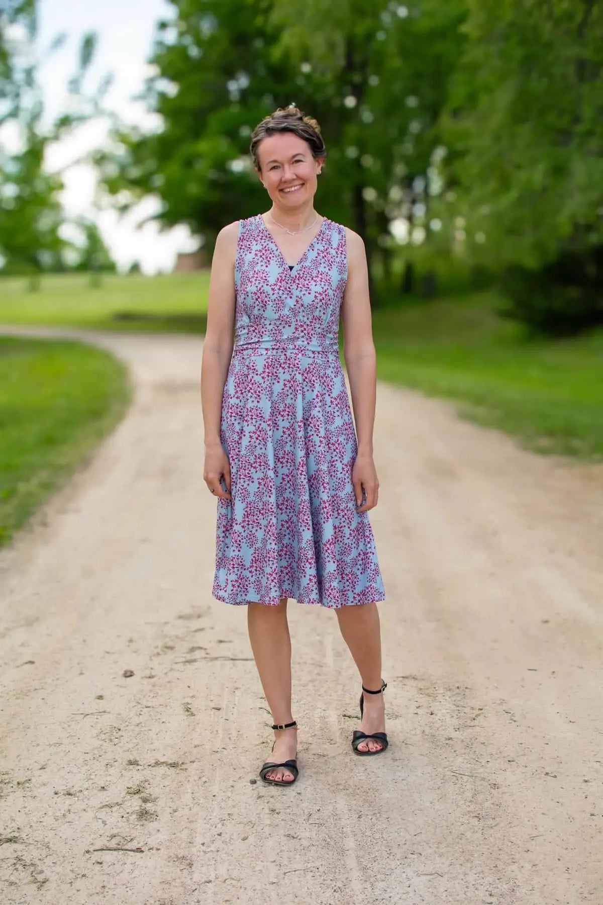 A woman in a blue and red floral dress stands on a dirt path.