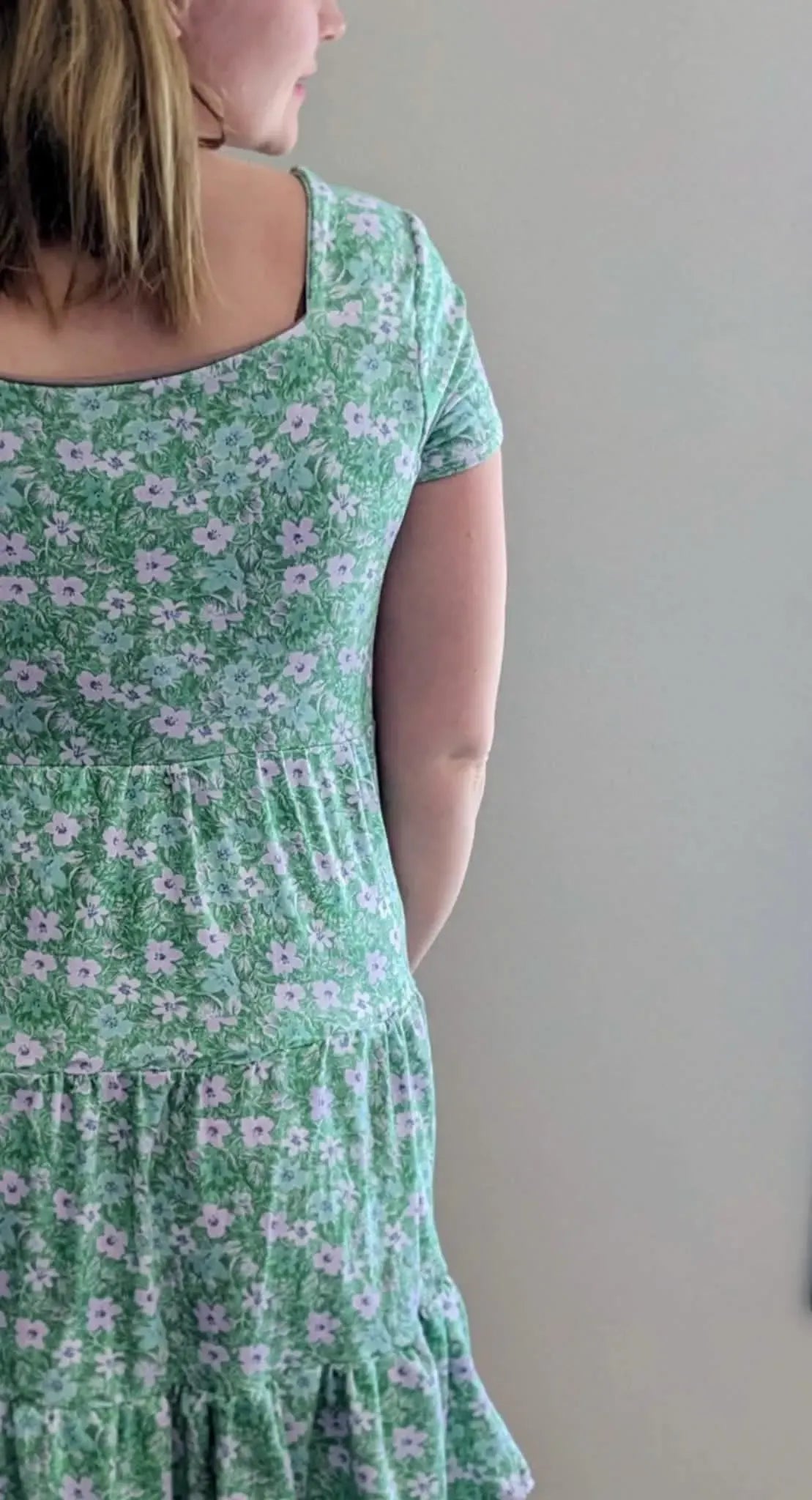 Woman in a green floral dress with a square neckline.