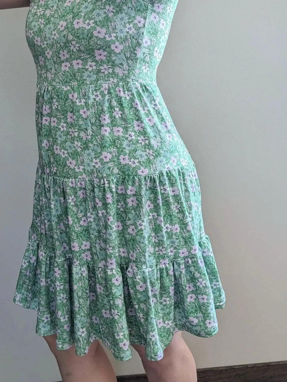 A person models a green floral dress with a tiered skirt.