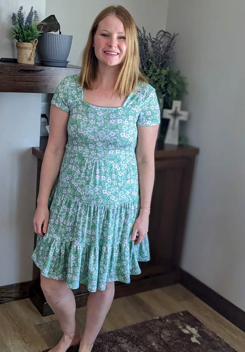 A woman in a green floral dress with a square neckline and ruffled hem.