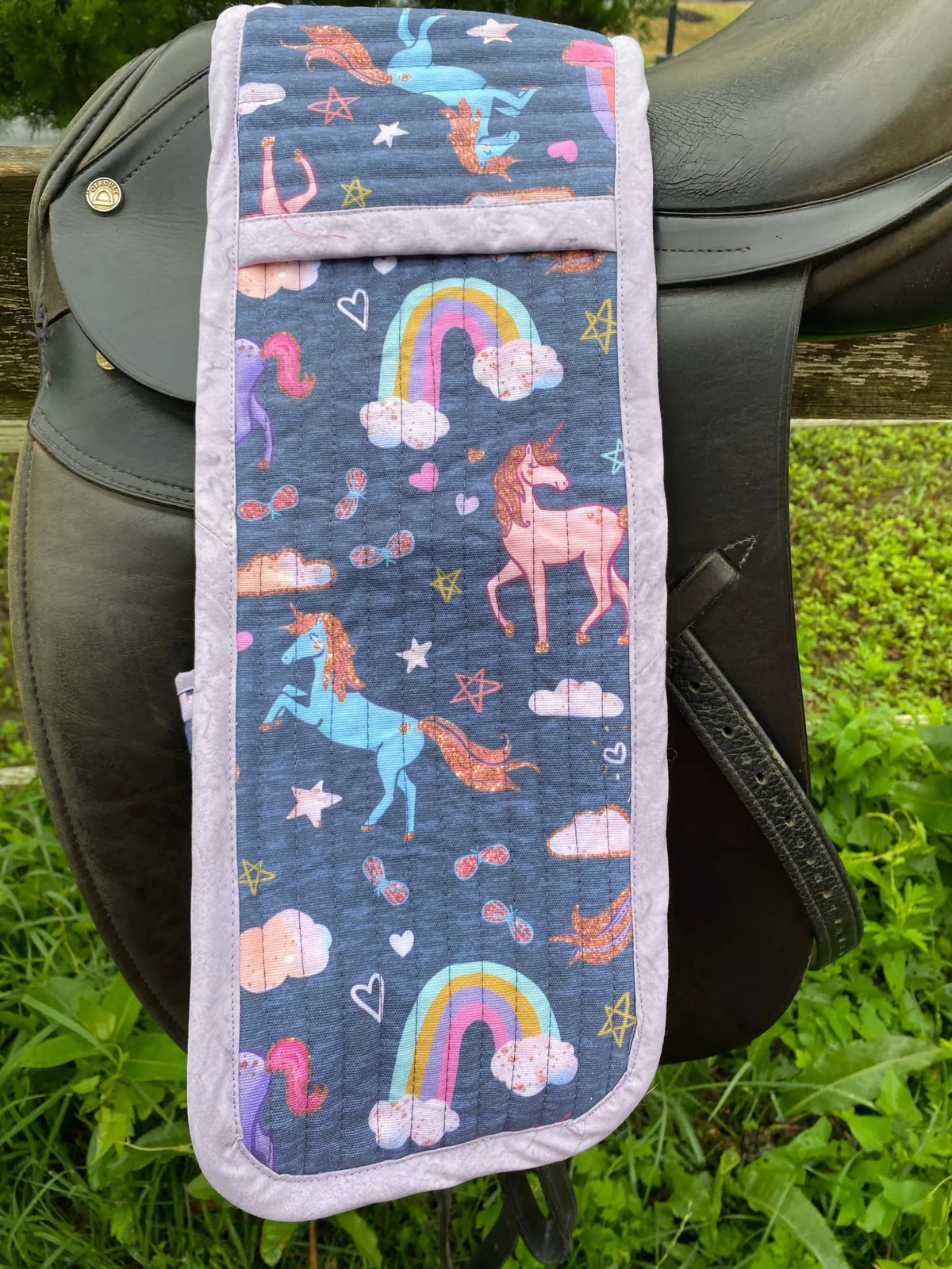 Navy unicorn fabric with rainbows and stars, draped over a black saddle.