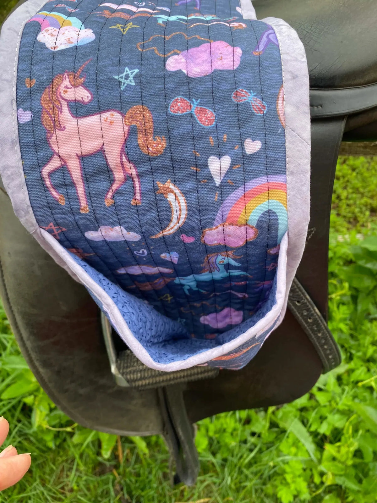 Navy unicorn fabric with rainbows and clouds, tucked into a saddle.