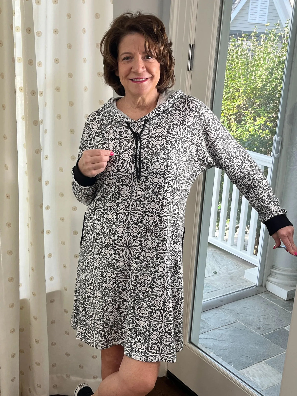 A woman smiles in a black and white patterned hoodie dress with black cuffs.