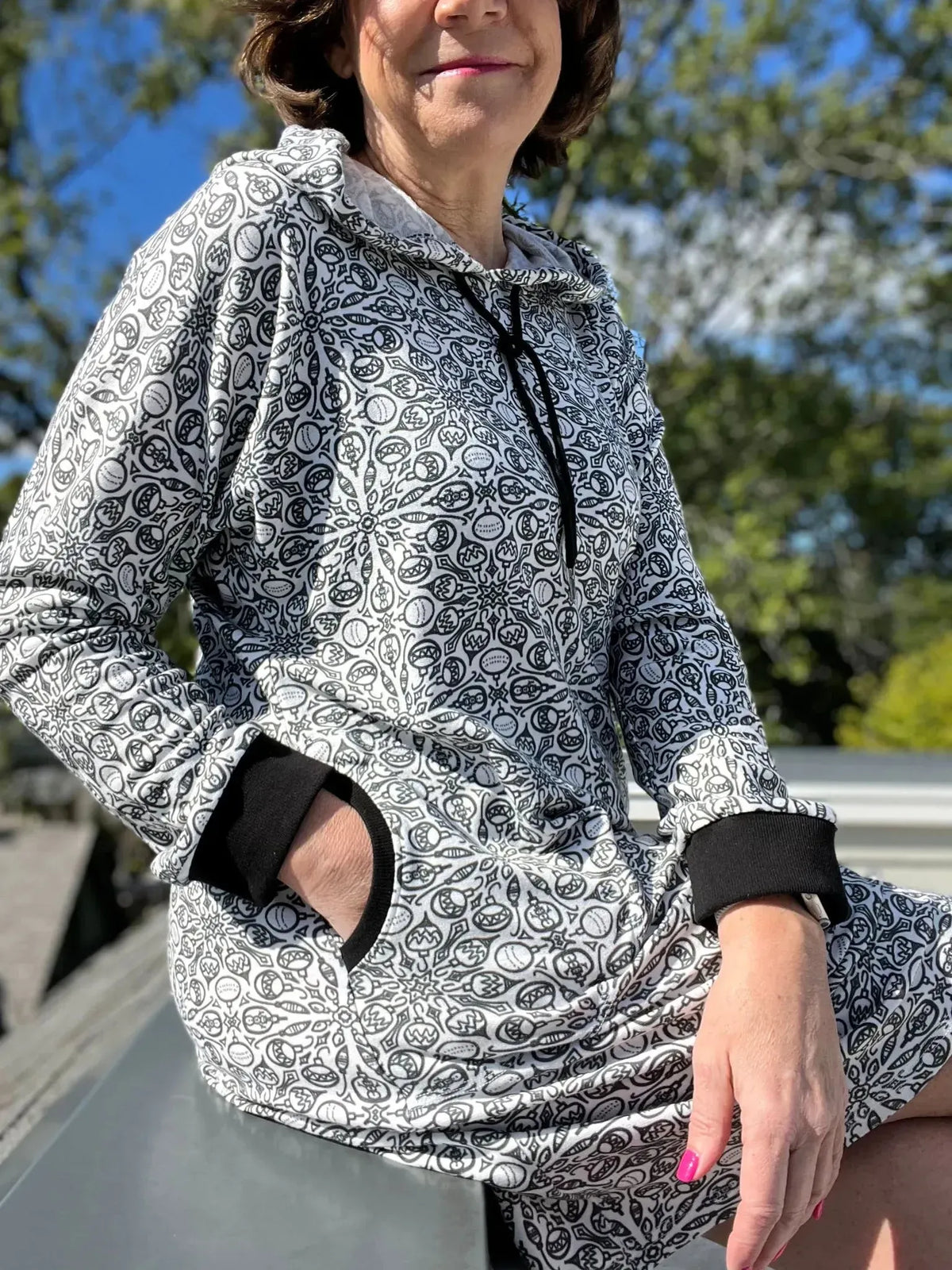 A woman wears a black and white Christmas sweater with a hood and black cuffs.