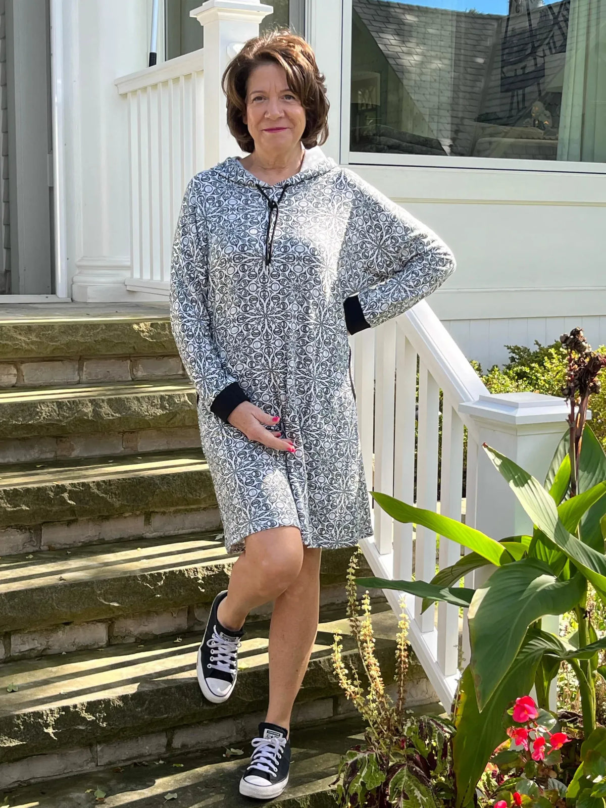 A woman in a patterned hooded dress and black sneakers stands on stone steps.