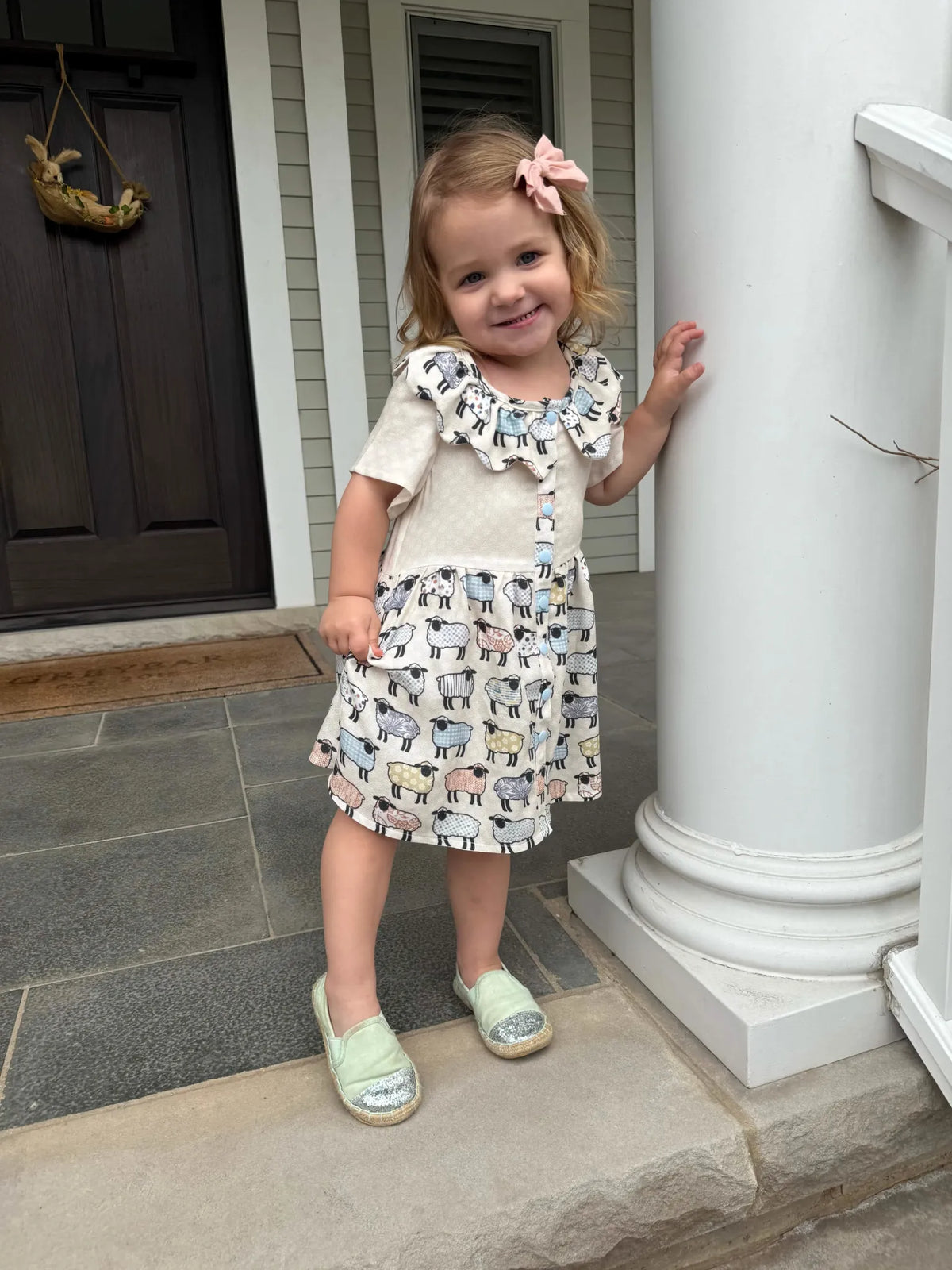 A young girl wears a dress with a patchwork sheep pattern.