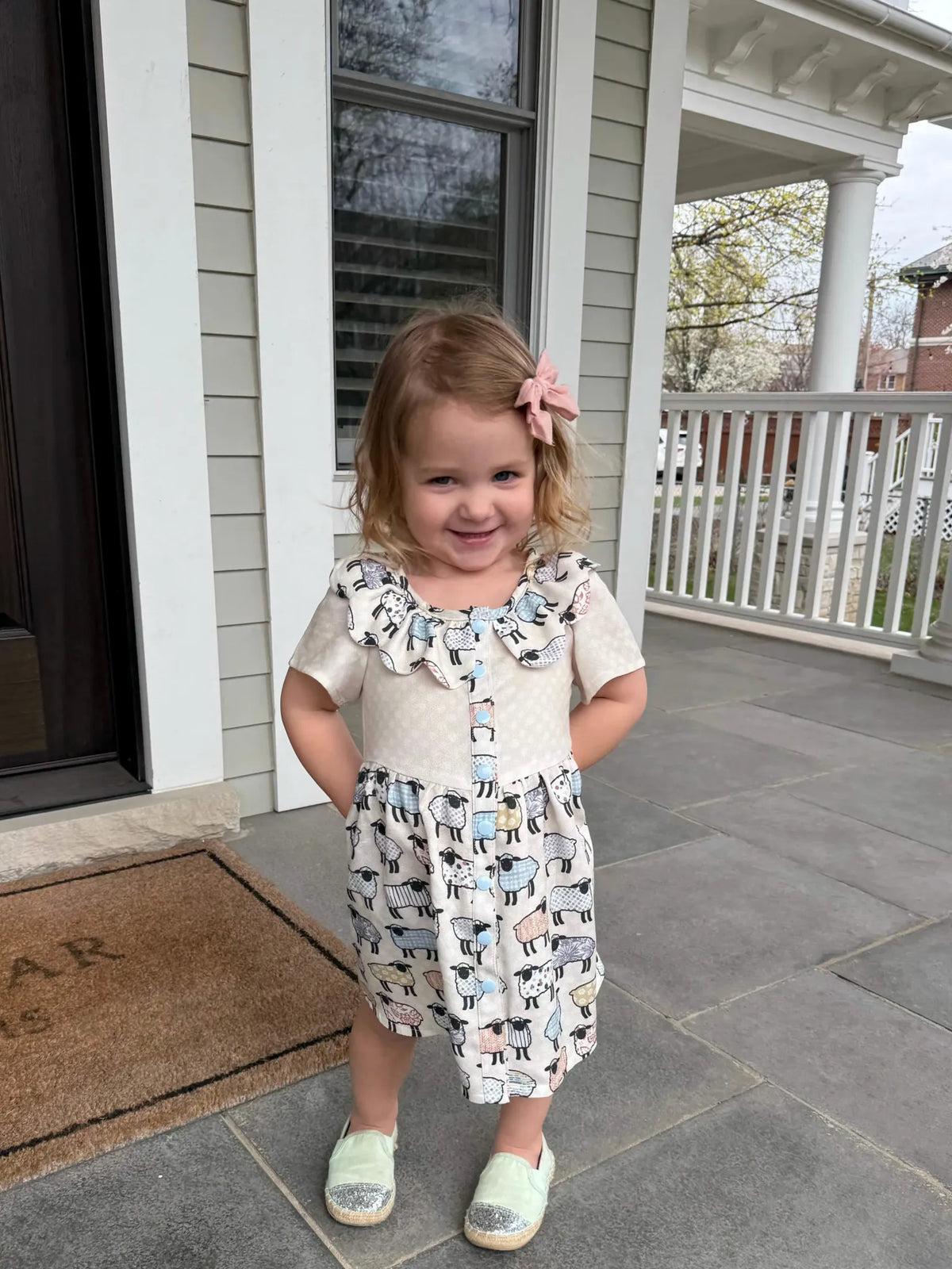 A young girl wears a dress with a patchwork sheep pattern.