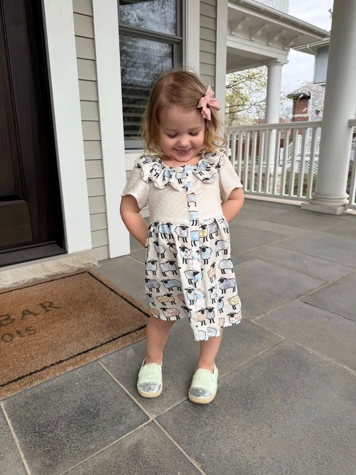 A young girl wears a dress with a patchwork sheep pattern.