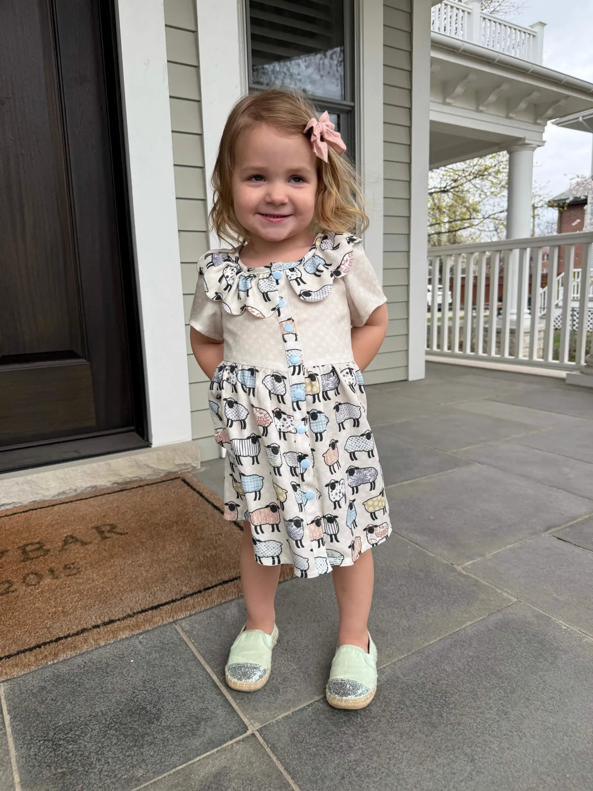 A young girl wears a dress with a patchwork sheep pattern.
