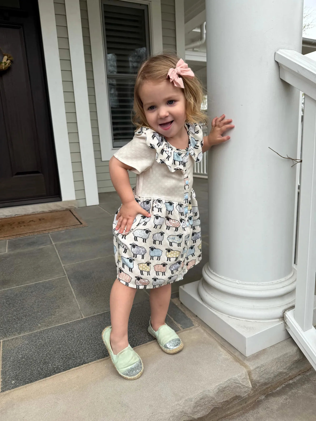 A young girl wears a dress with a patchwork sheep pattern.