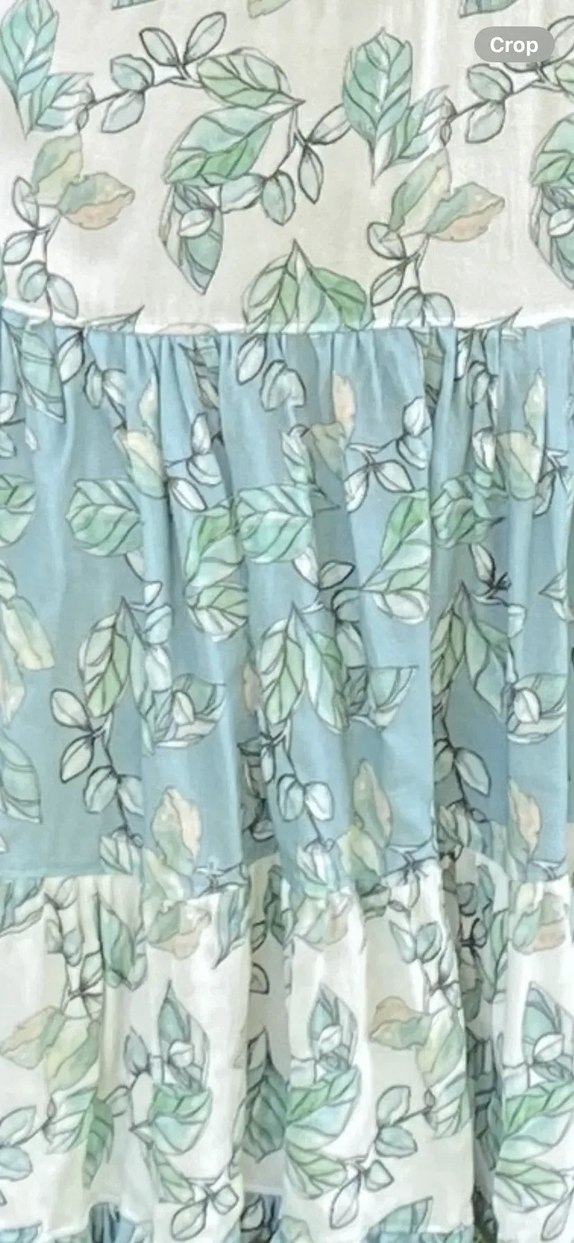 Fabric with a pattern of green leaves on white and blue ruffled tiers.