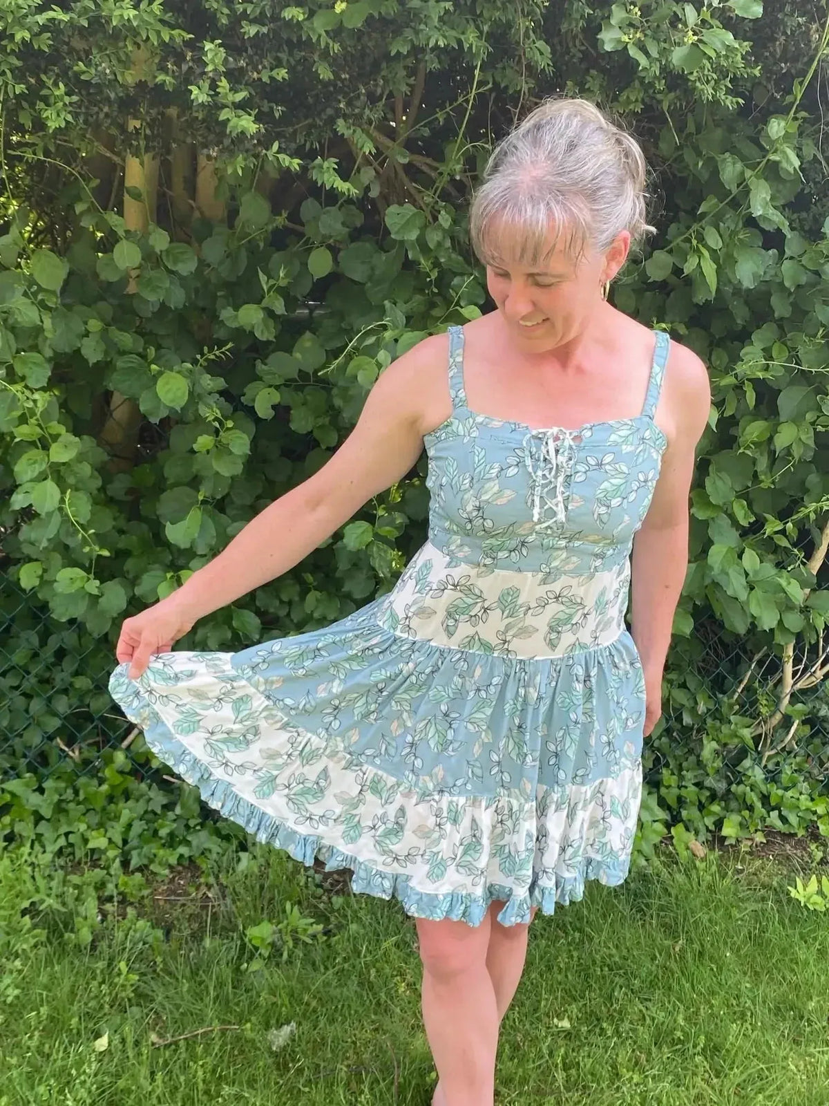 Woman modeling a short blue and white eucalyptus leaf print dress outdoors.