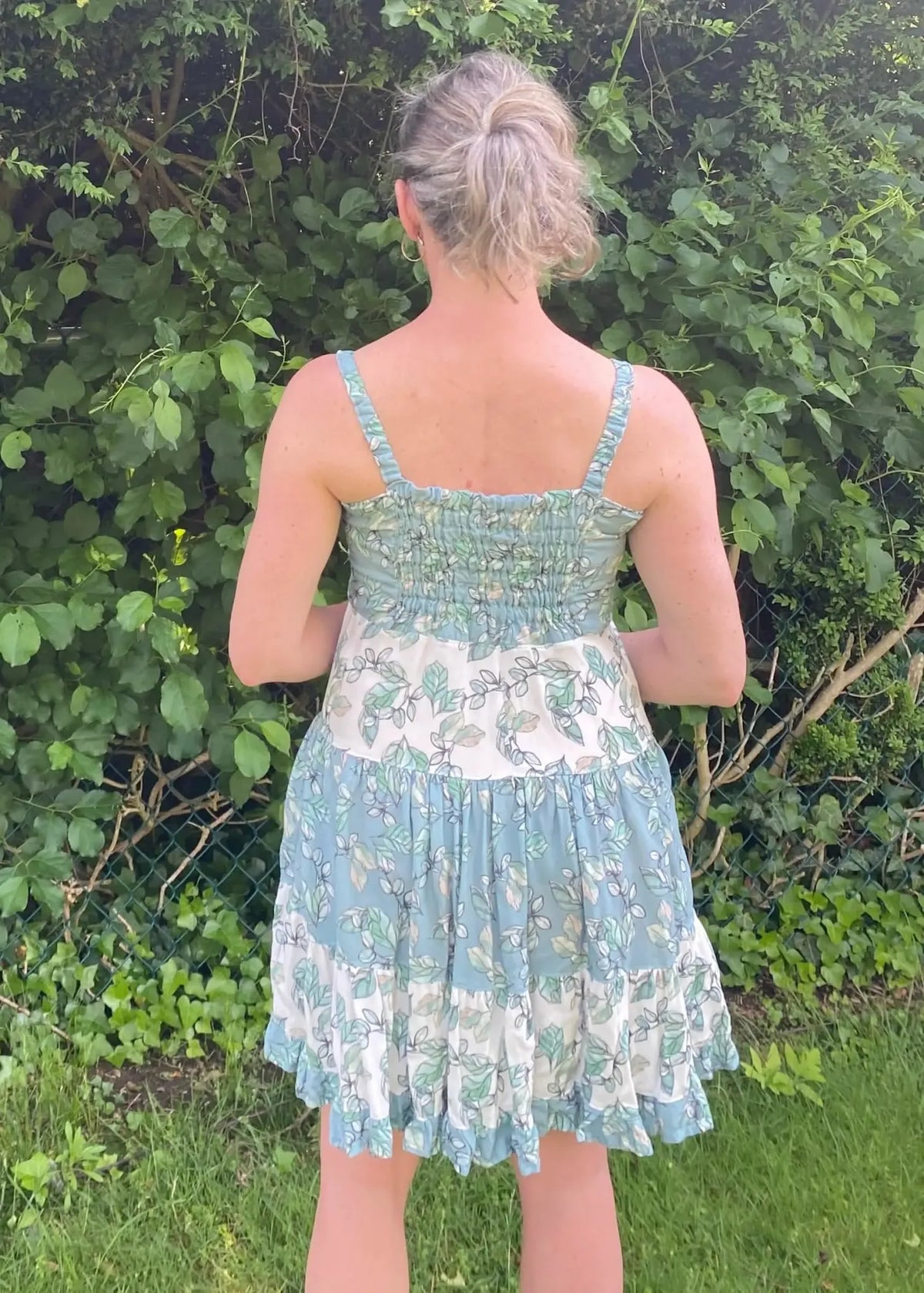 A woman from behind wears a blue and white floral dress with a smocked bodice.