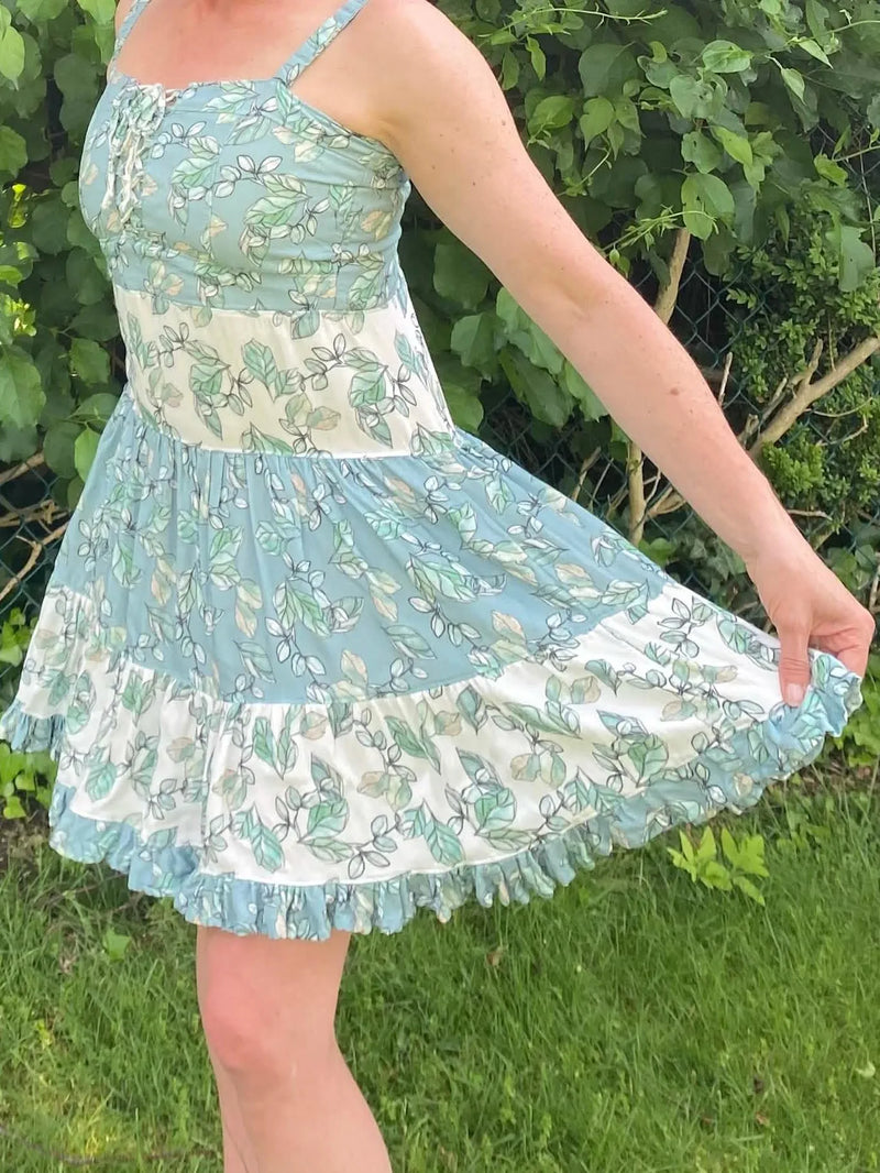 A woman models a Willow Mist dress with a leaf pattern and ruffled hem.