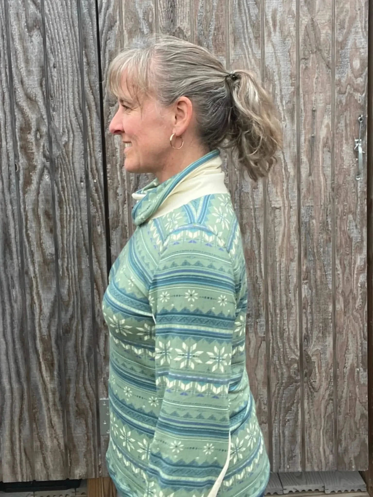 A woman in a green and blue patterned top with a cream collar smiles in profile.