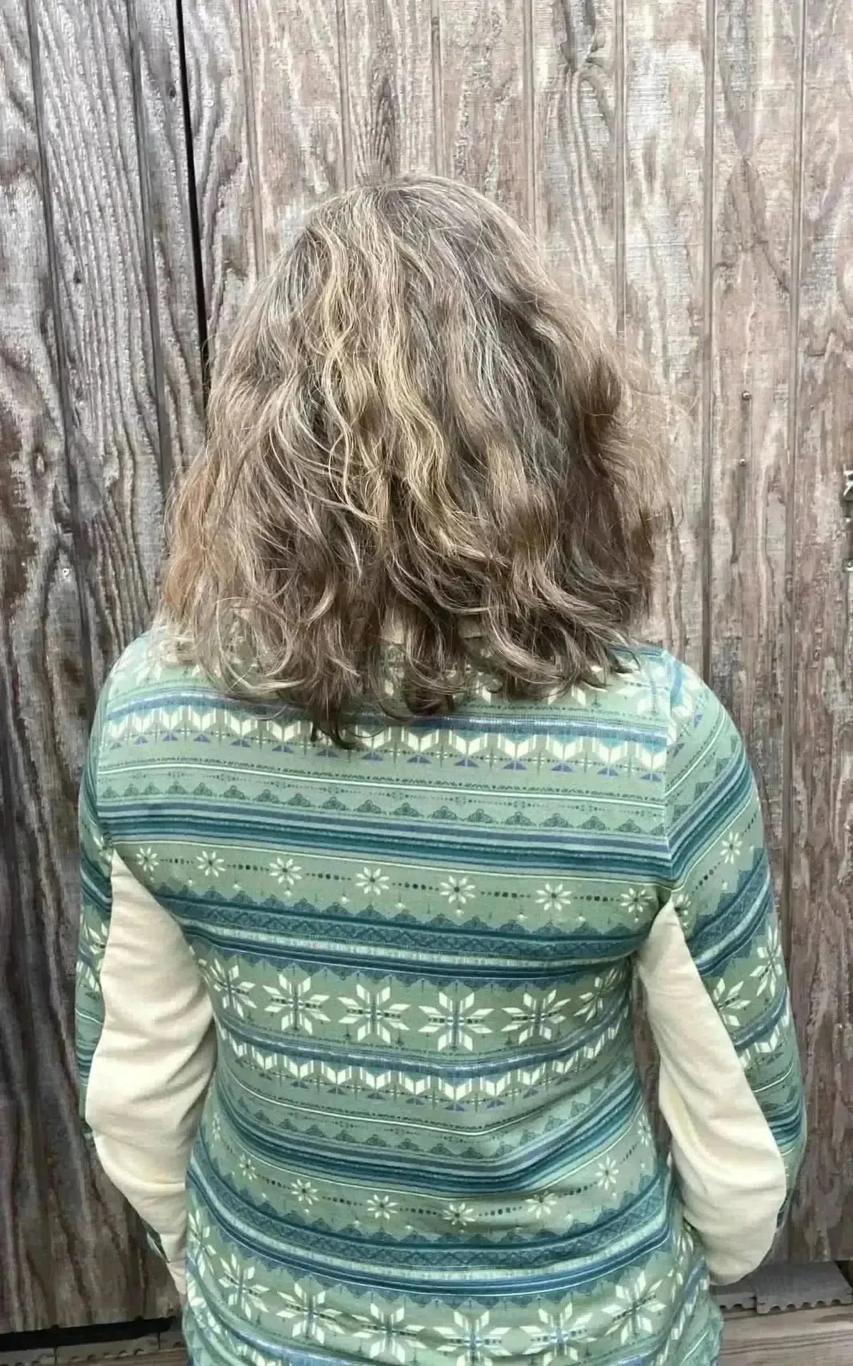 Back view of green-blue winter snowflake print fabric on a garment against a wooden wall.