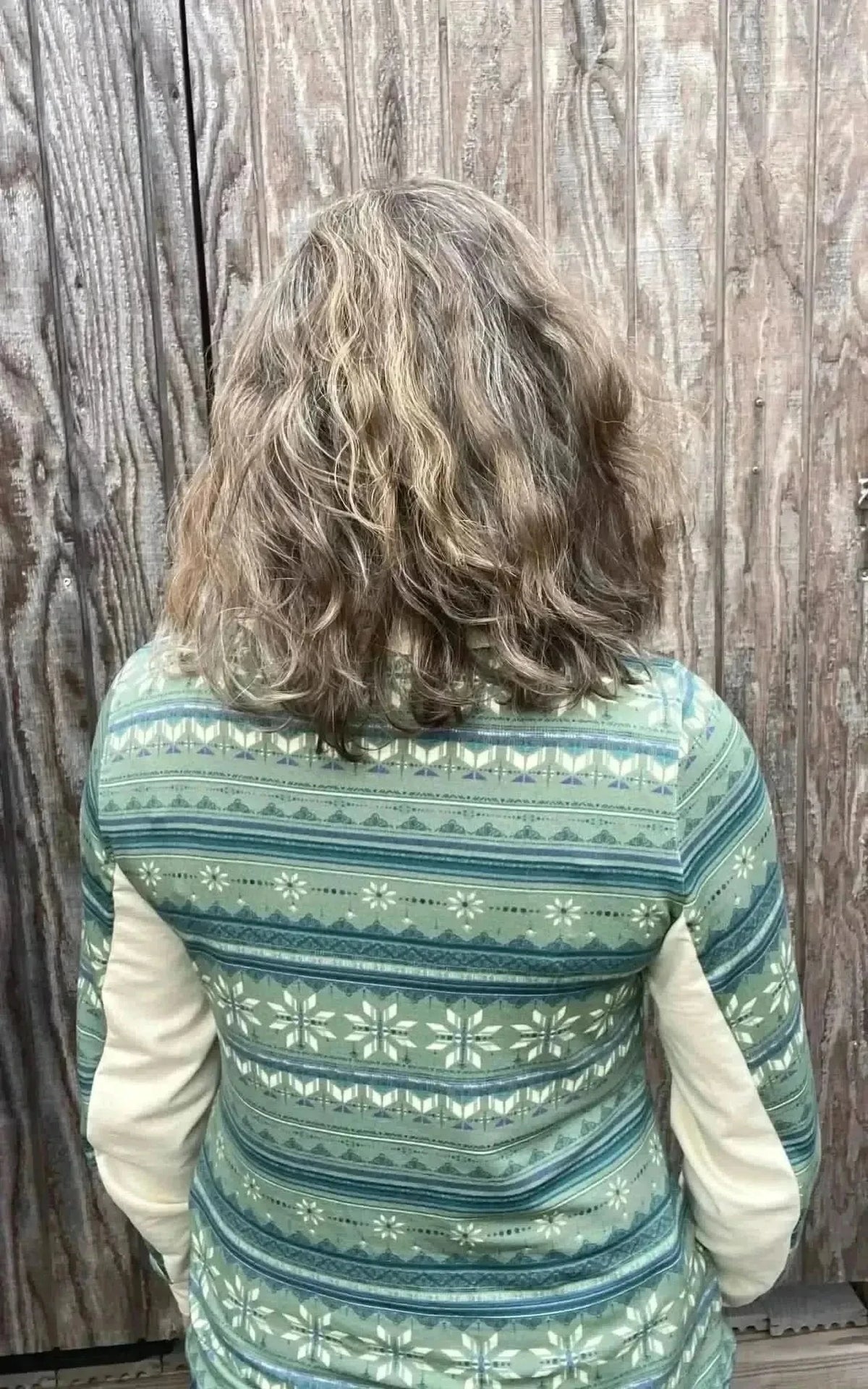 Back view of green-blue winter snowflake print fabric on a garment against a wooden wall.