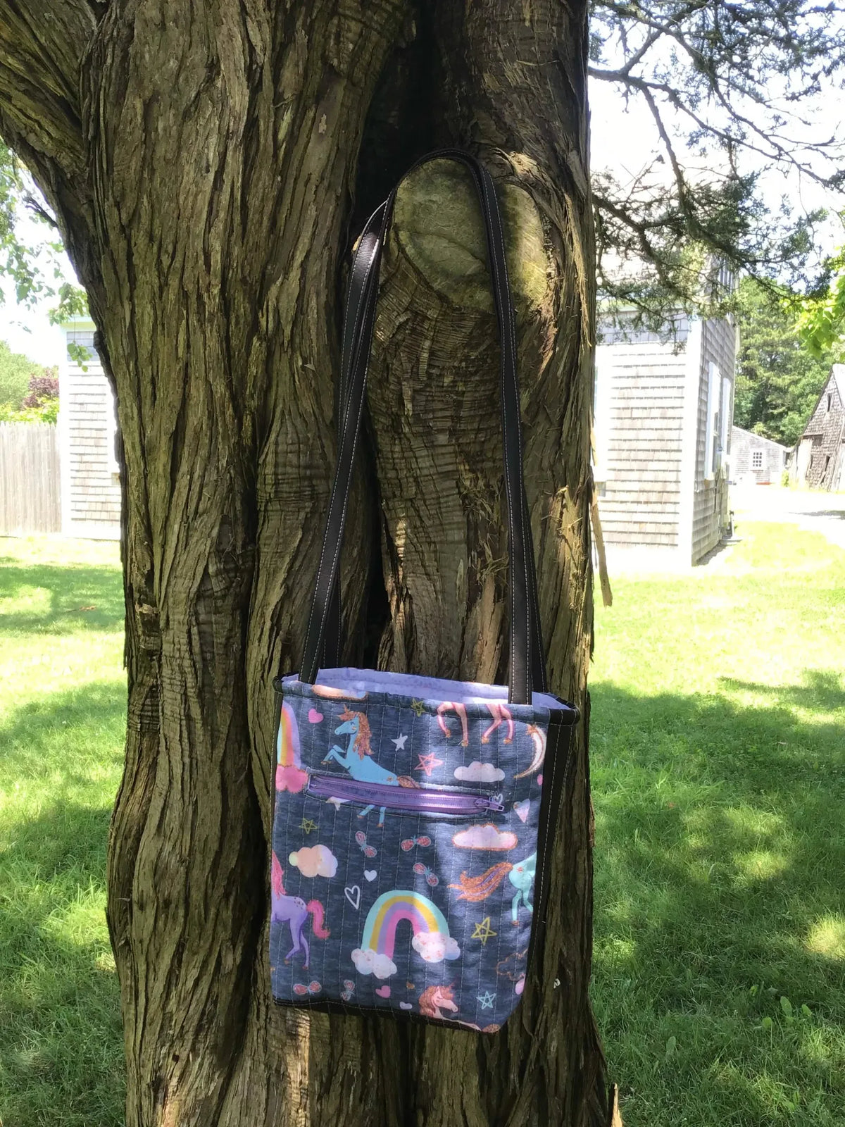 Navy Unicorn bag with a purple zipper hanging on a tree.