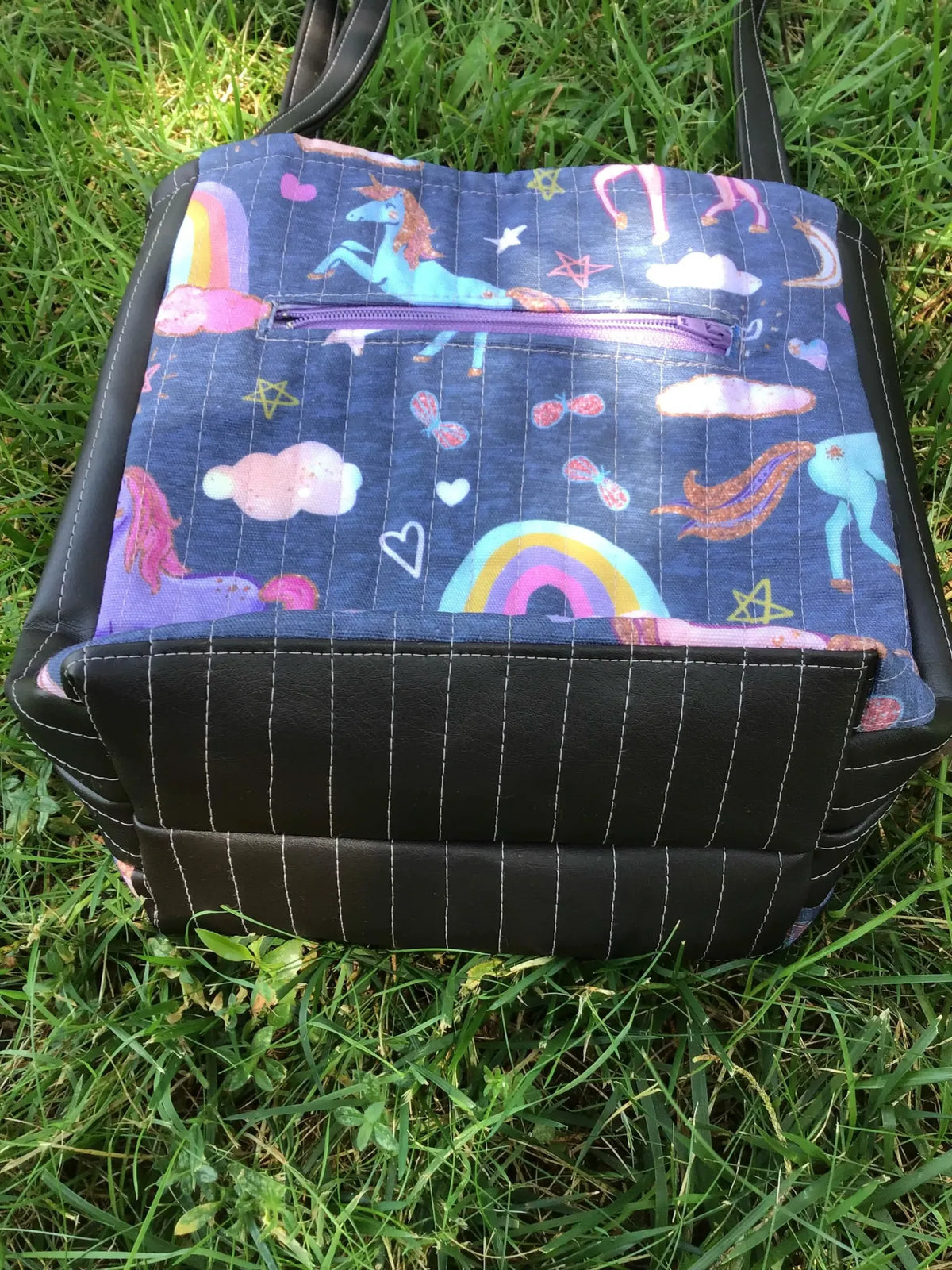 Navy unicorn fabric tote bag with black base and white stitching on green grass.