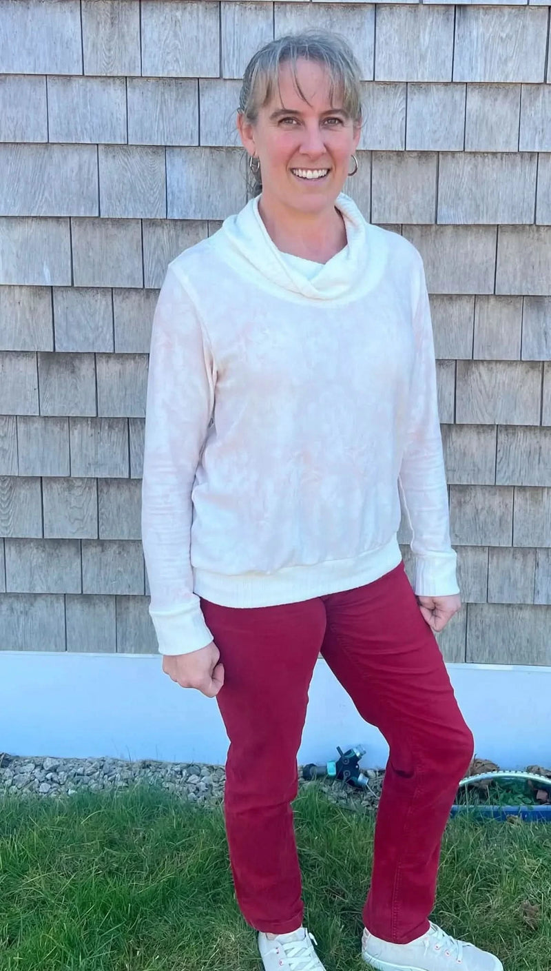 A woman wears a light pink floral cowl neck top and red pants.