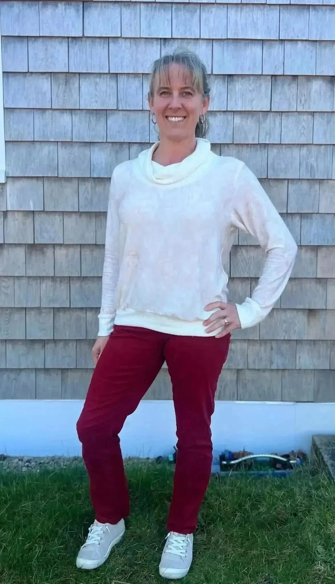 Woman modeling pink floral print fabric as a white cowl-neck top with red pants.