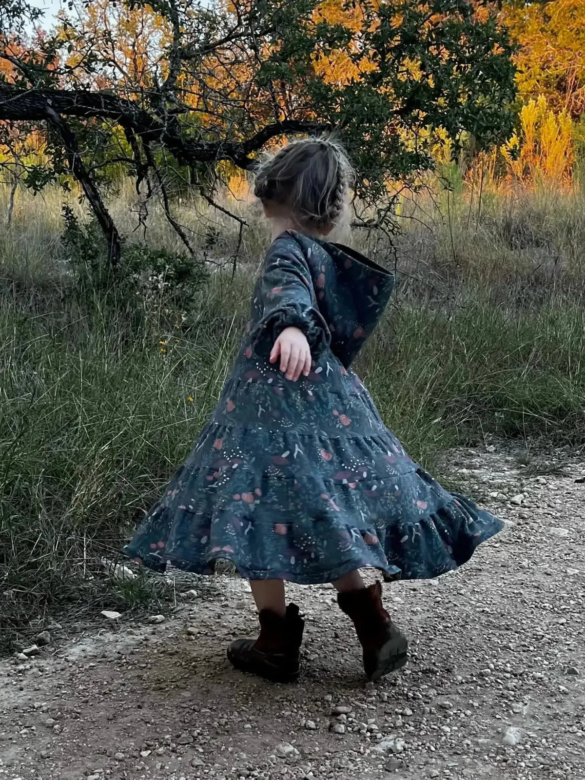Girl in navy botanical print dress with hood twirling in autumn field.