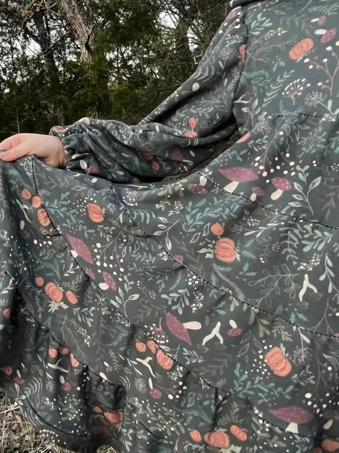 Green botanical print fabric with forest foliage, mushrooms, and berries on a dark green background.