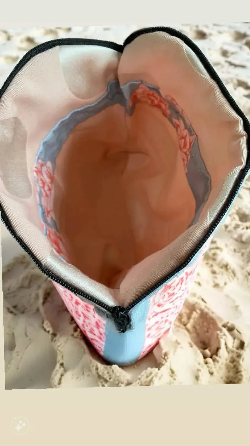 A fabric pouch with a floral pattern and a zipper stands in the sand.