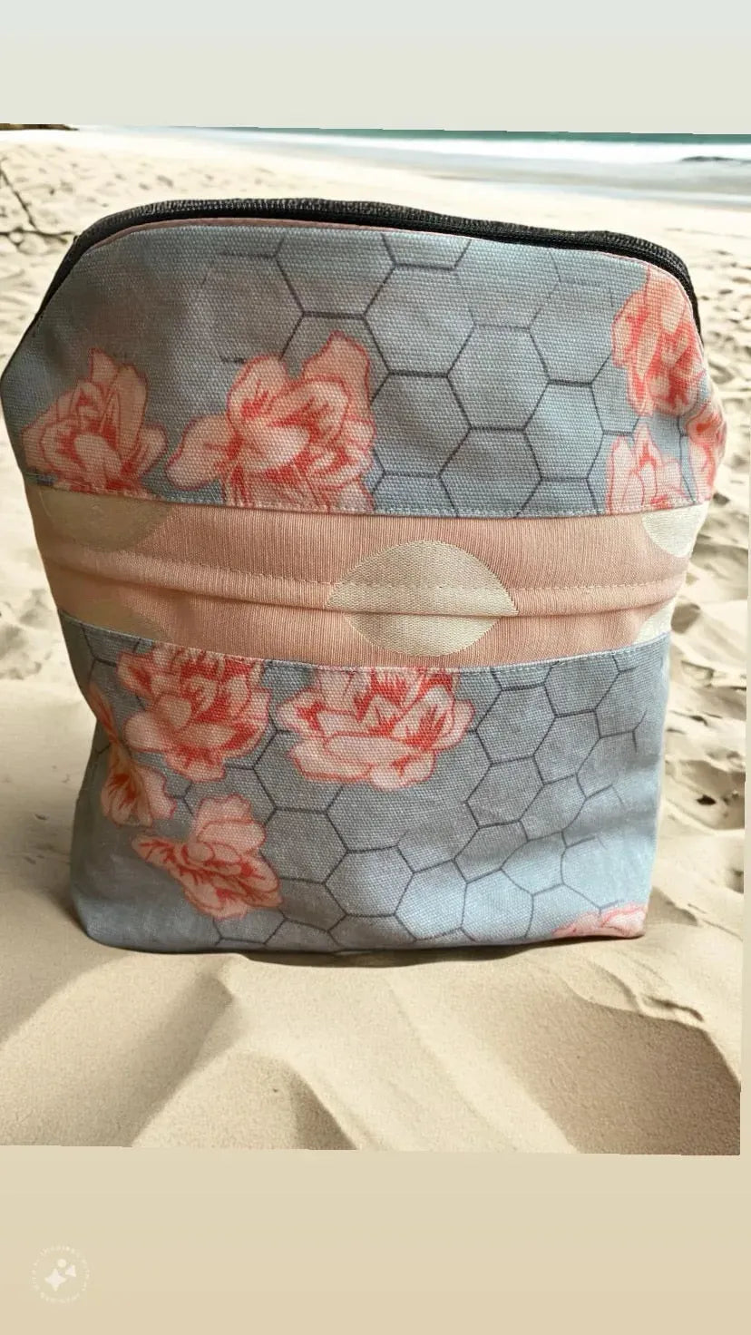 A fabric pouch with a honeycomb and floral pattern sits on sand.