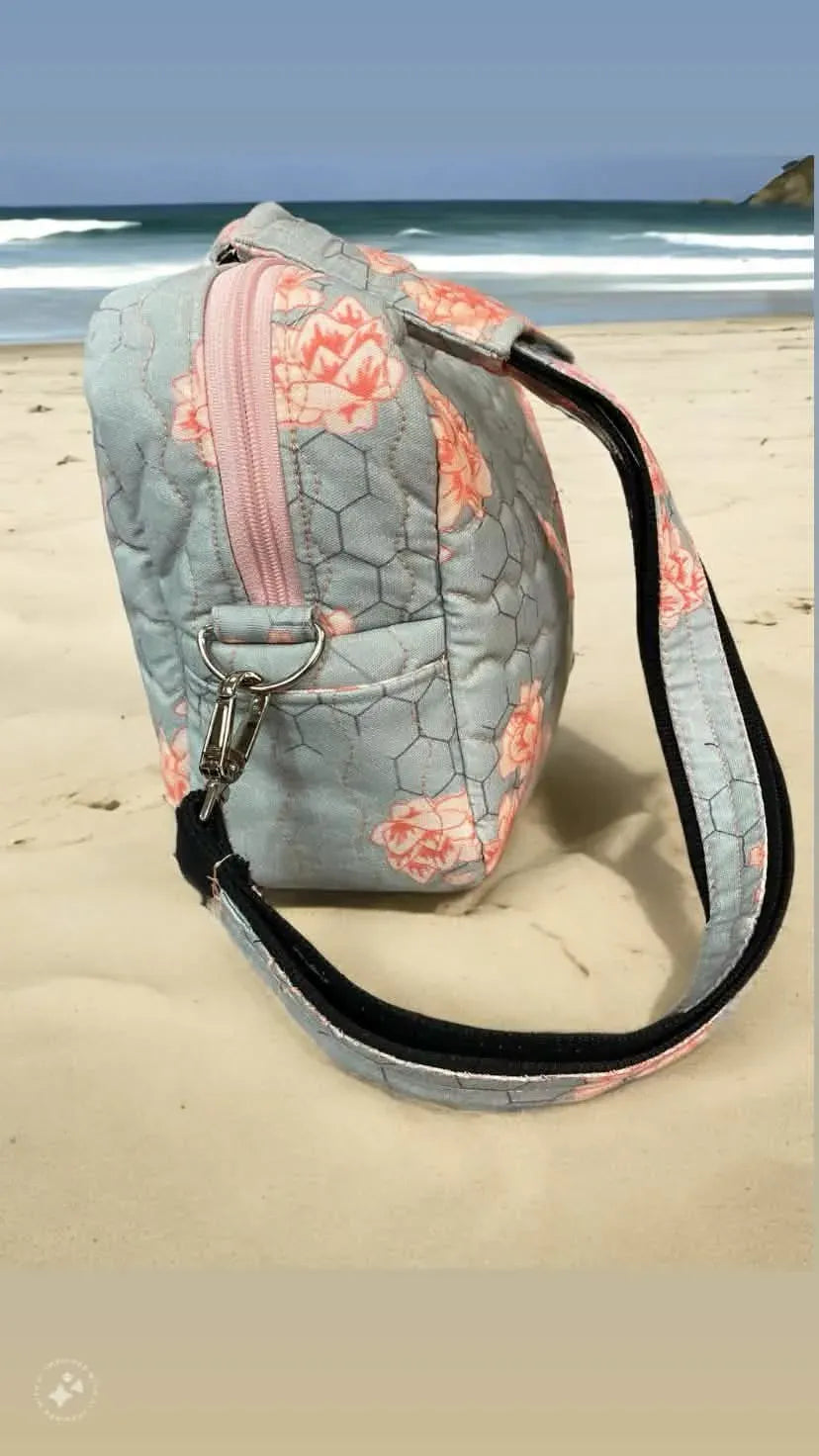 A quilted bag with a honeycomb and floral pattern sits on a sandy beach.