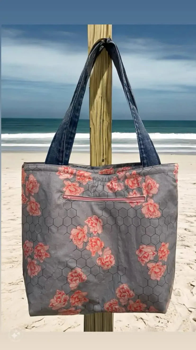 A gray tote bag with a honeycomb and pink floral pattern hangs on a wooden post.