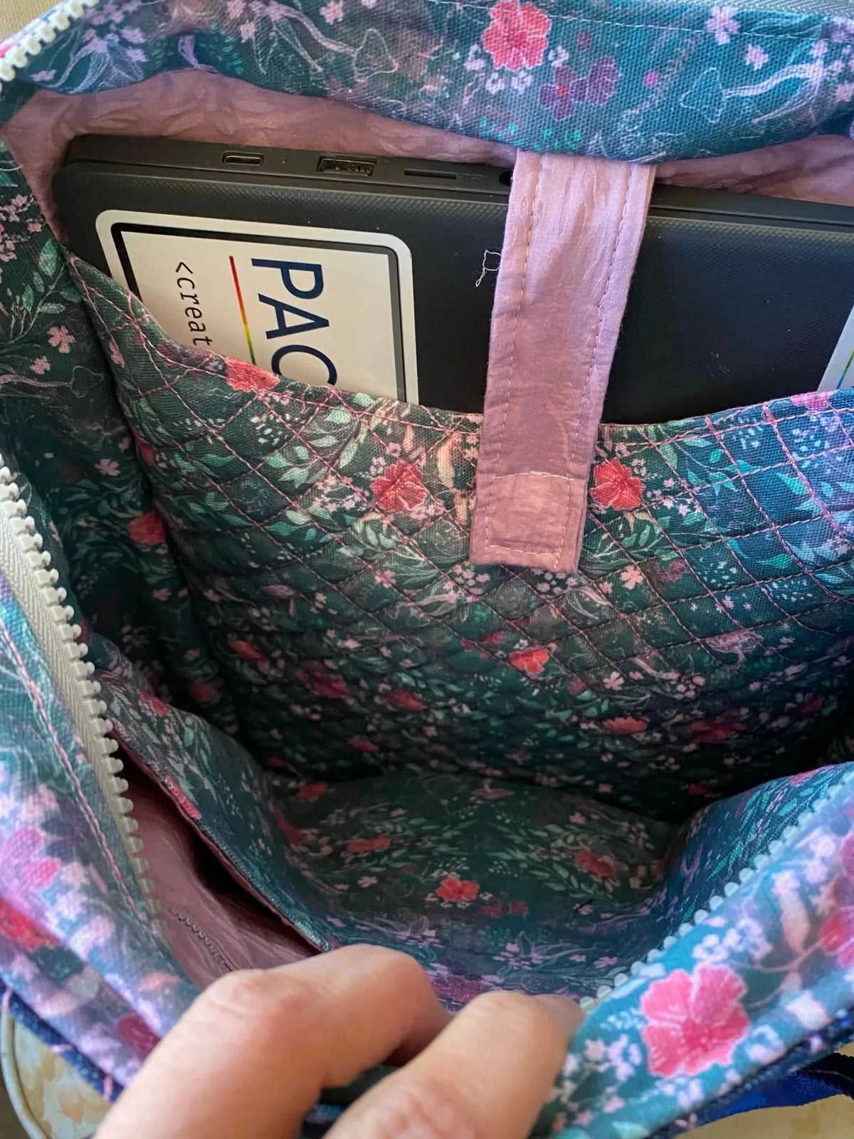 A quilted floral fabric bag holds a black tablet with a "PAC" sticker.