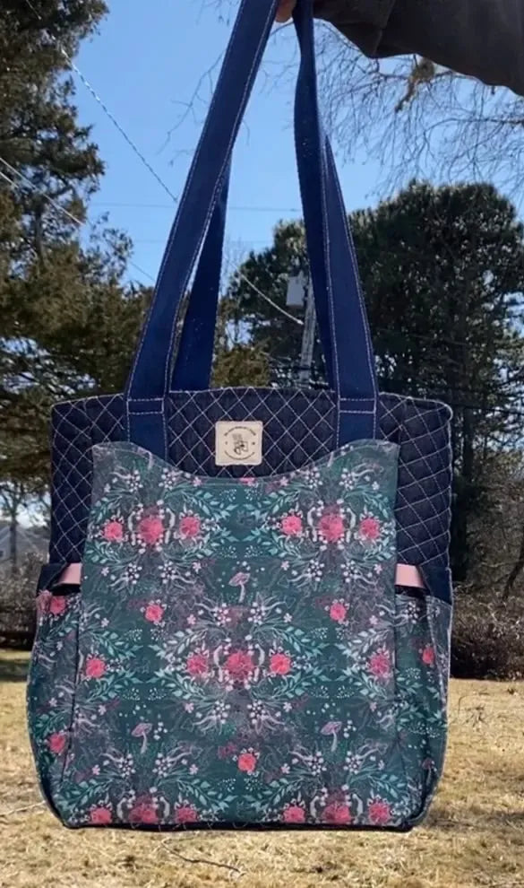 A quilted tote bag with a dark floral pattern and solid navy straps.
