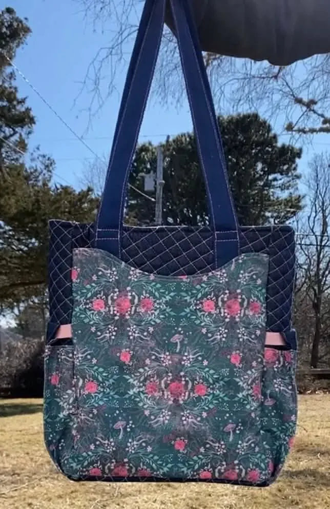A dark blue quilted tote bag with a floral and mushroom patterned front pocket.