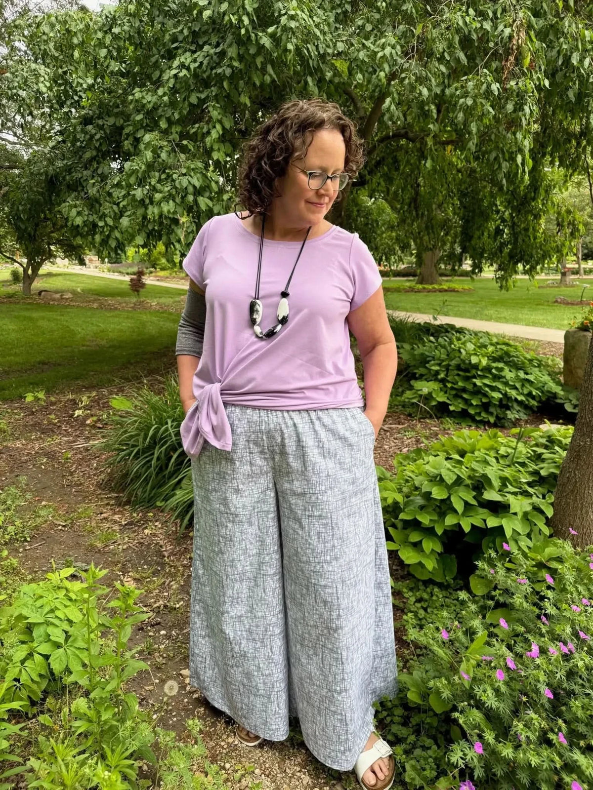 A woman wears wide-leg pants with a black hatch pattern and a lavender top.