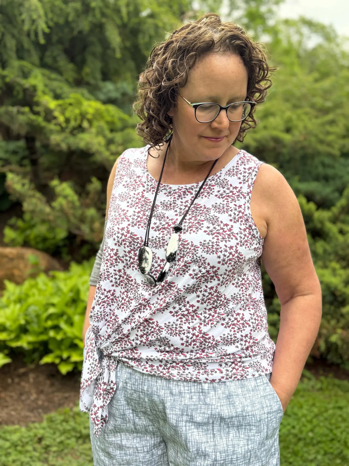 A woman in a floral top and patterned pants stands outdoors.