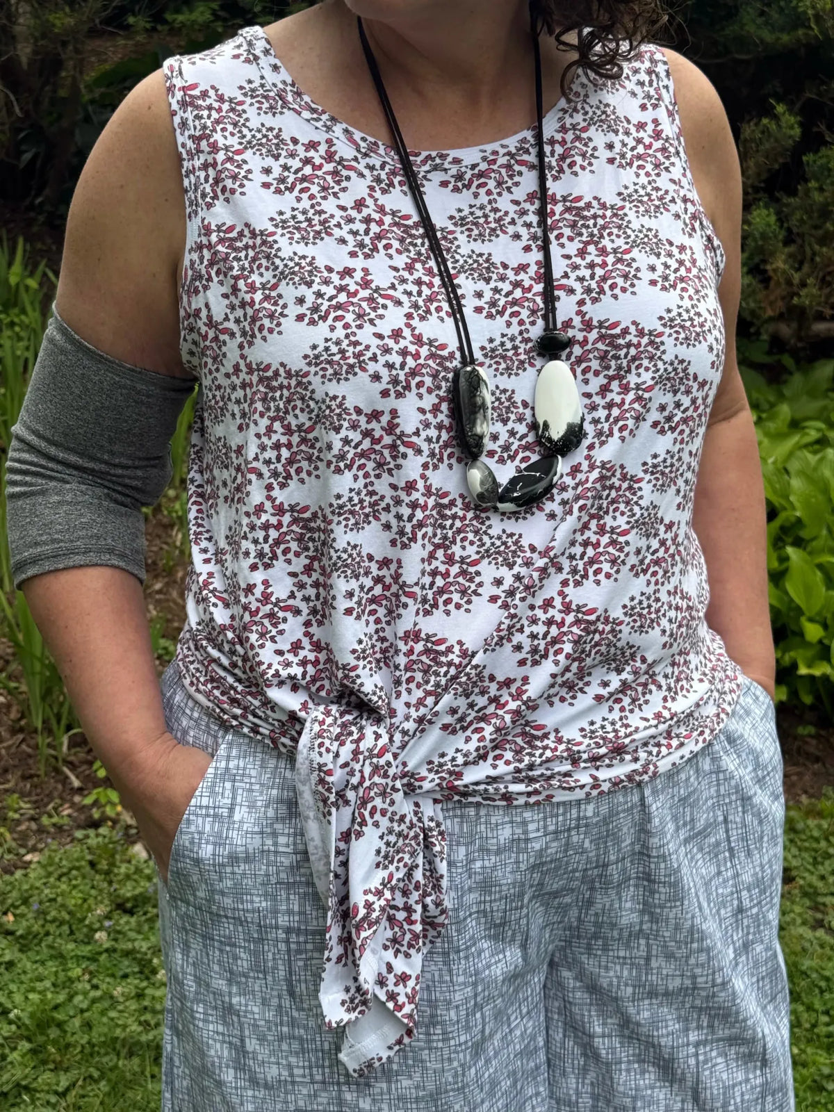 A person wears a white tank top with red floral print and light gray patterned pants.