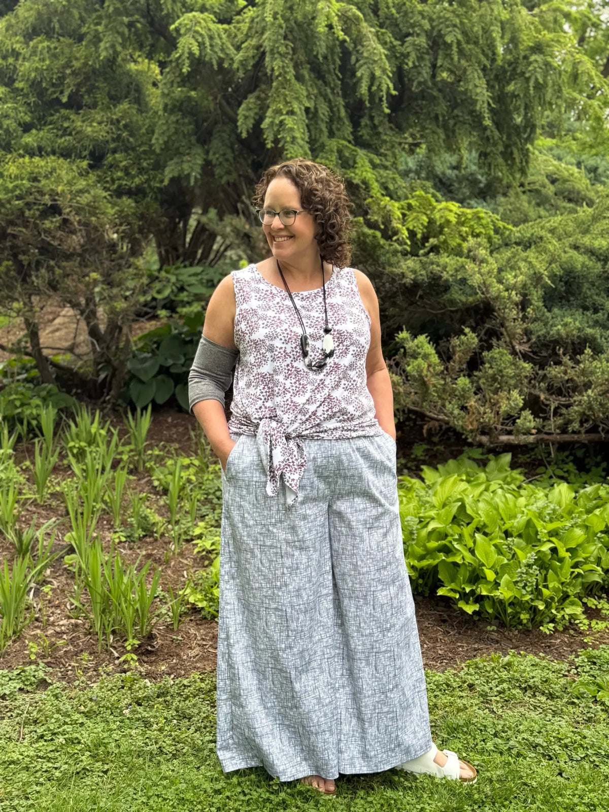 A woman wears a white and black patterned top with light gray patterned wide-leg pants.