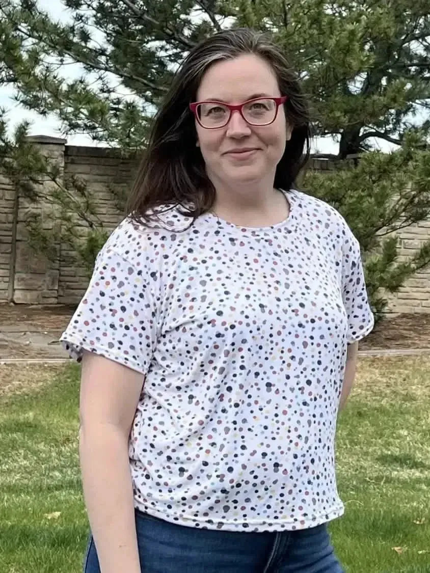White short-sleeve T-shirt with multicolored confetti dots print on a woman outdoors.