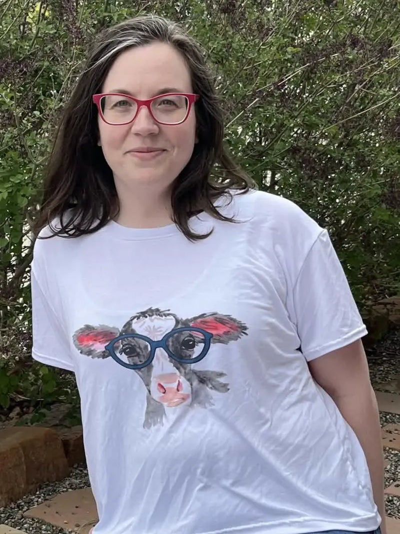 A woman wears a white t-shirt with a graphic of a calf wearing blue glasses.
