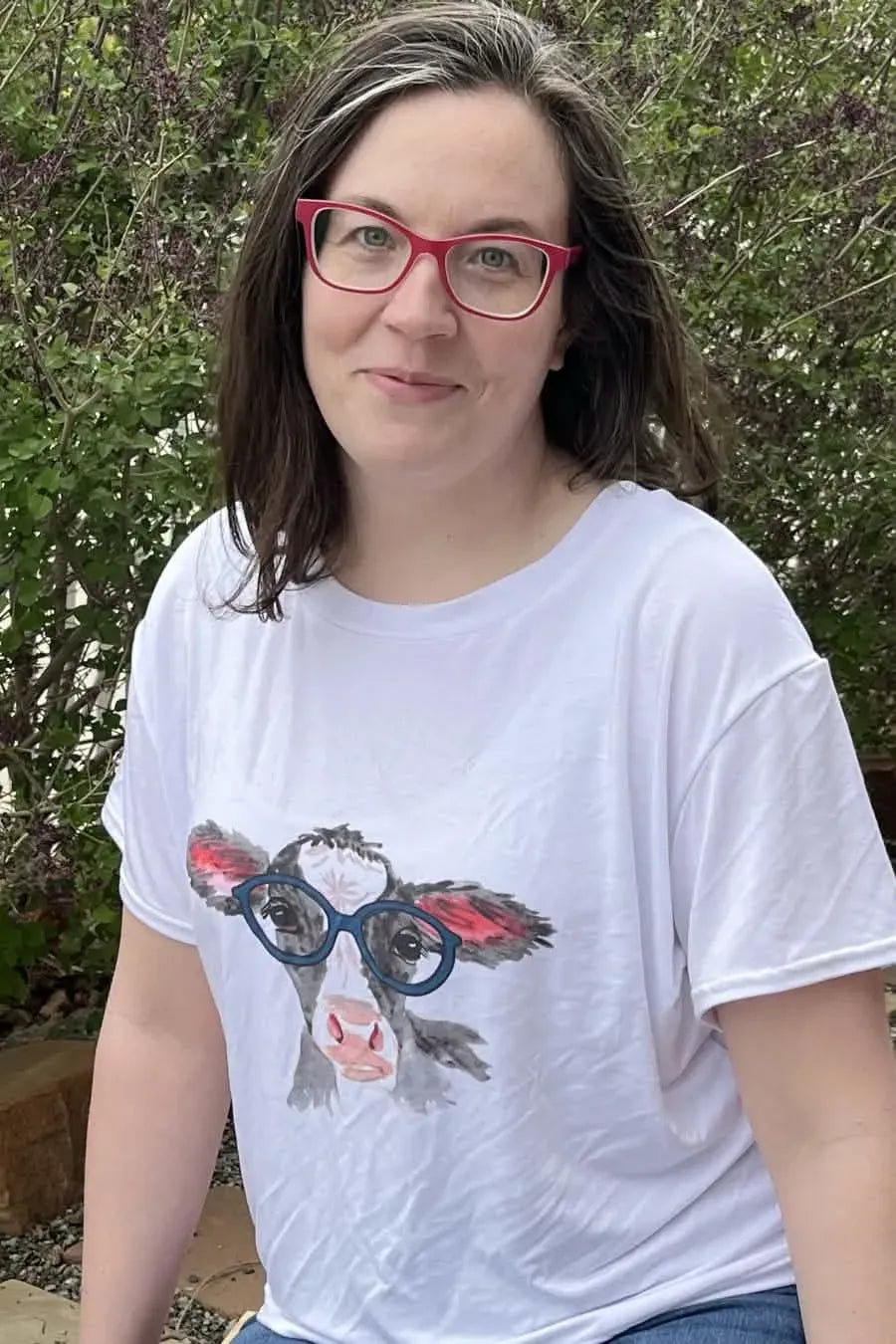 A woman wears a white t-shirt with a graphic of a cow wearing blue glasses.
