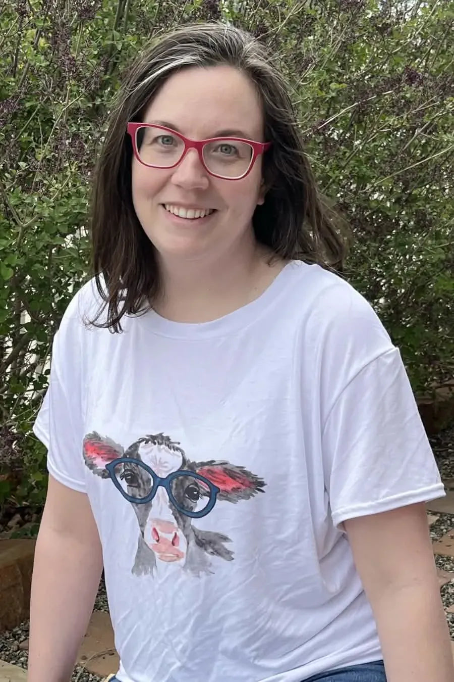 A woman wears a white t-shirt with a graphic of a cow wearing blue glasses.