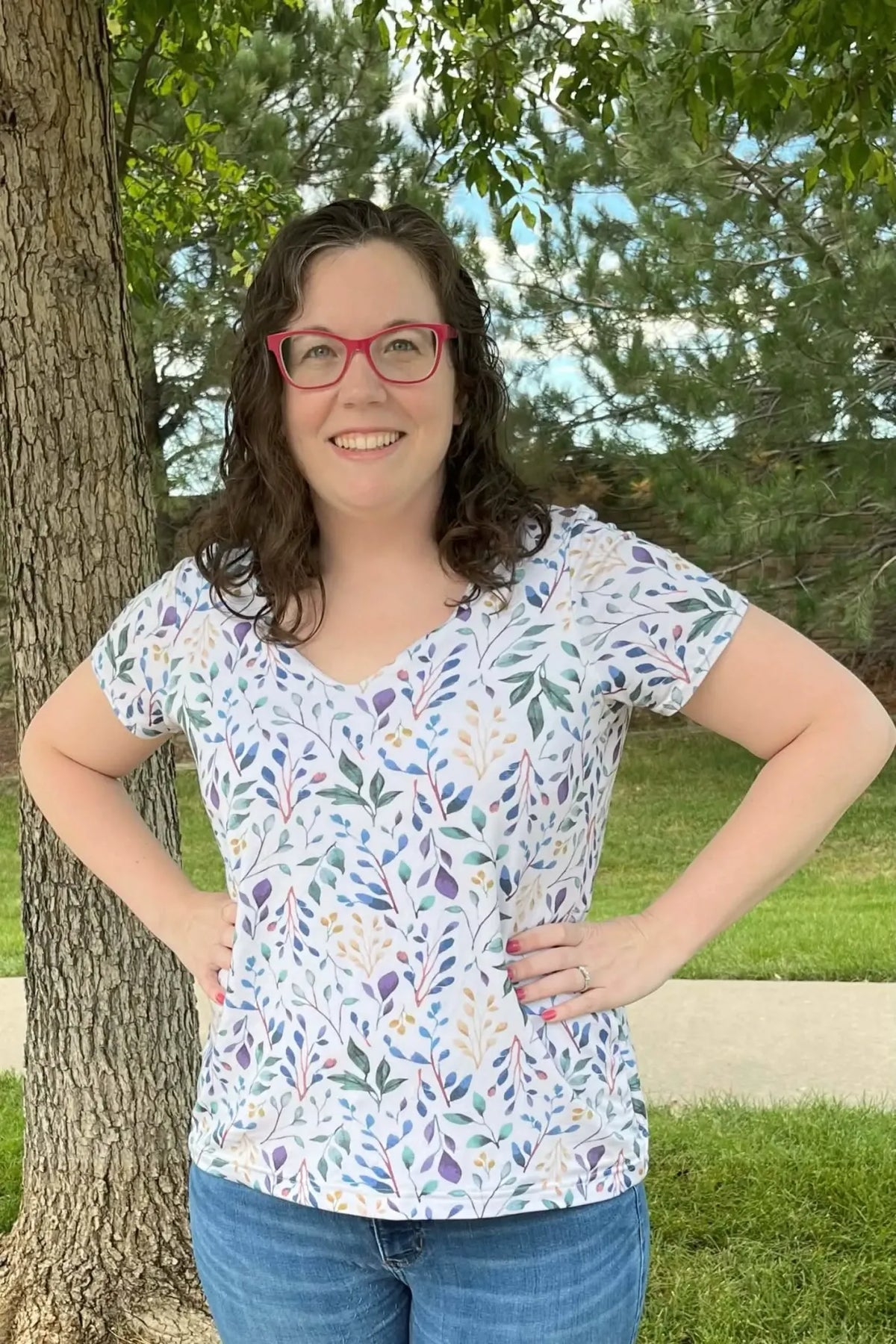 A woman in a white shirt with a colorful leaf pattern and blue jeans smiles at the camera.