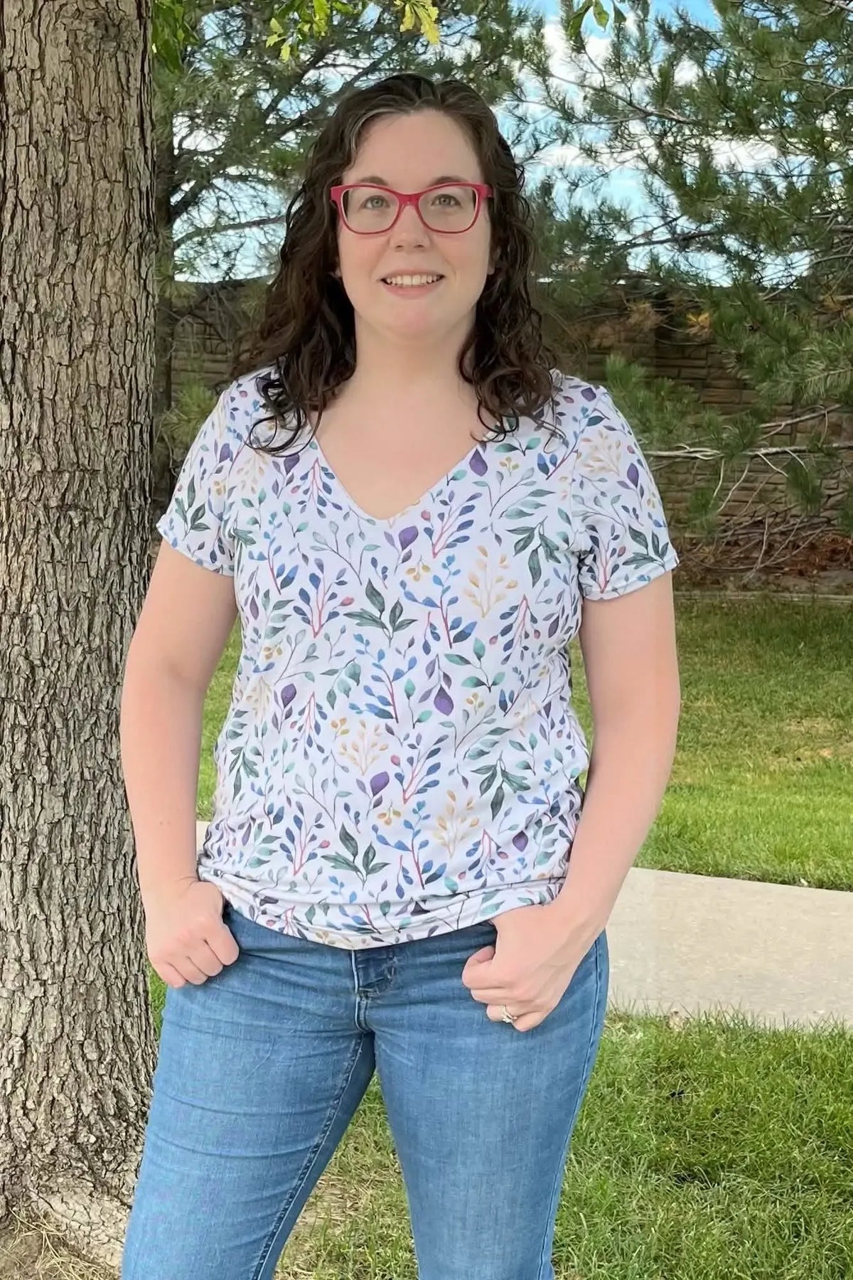 Woman in a v-neck shirt with a colorful leaf pattern and blue jeans.