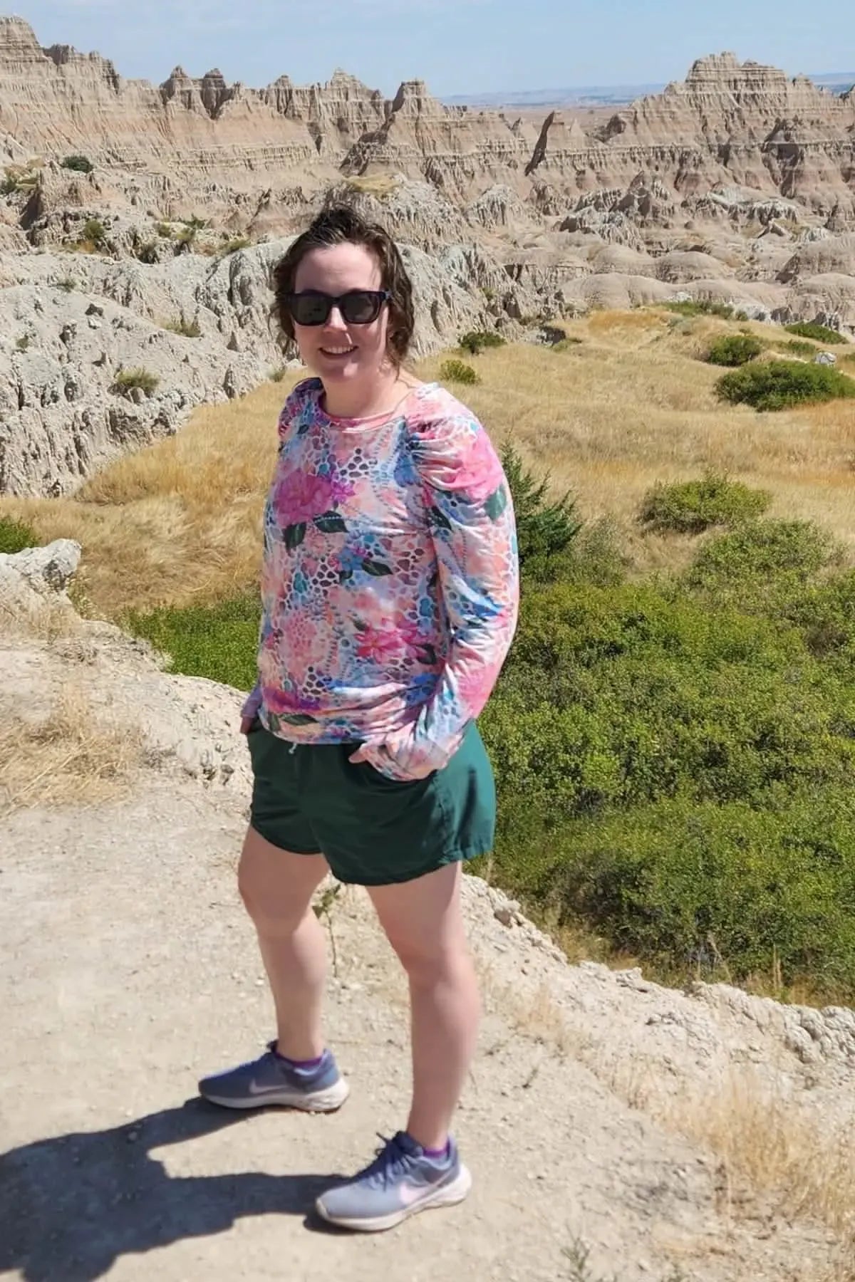 A woman in a floral long-sleeved shirt and shorts stands in a desert landscape.