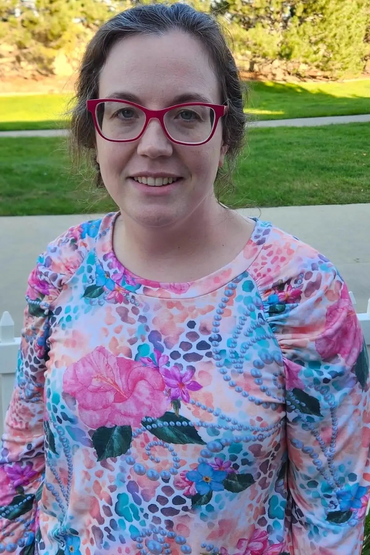 A woman wearing a colorful floral and pearl print long-sleeved shirt.