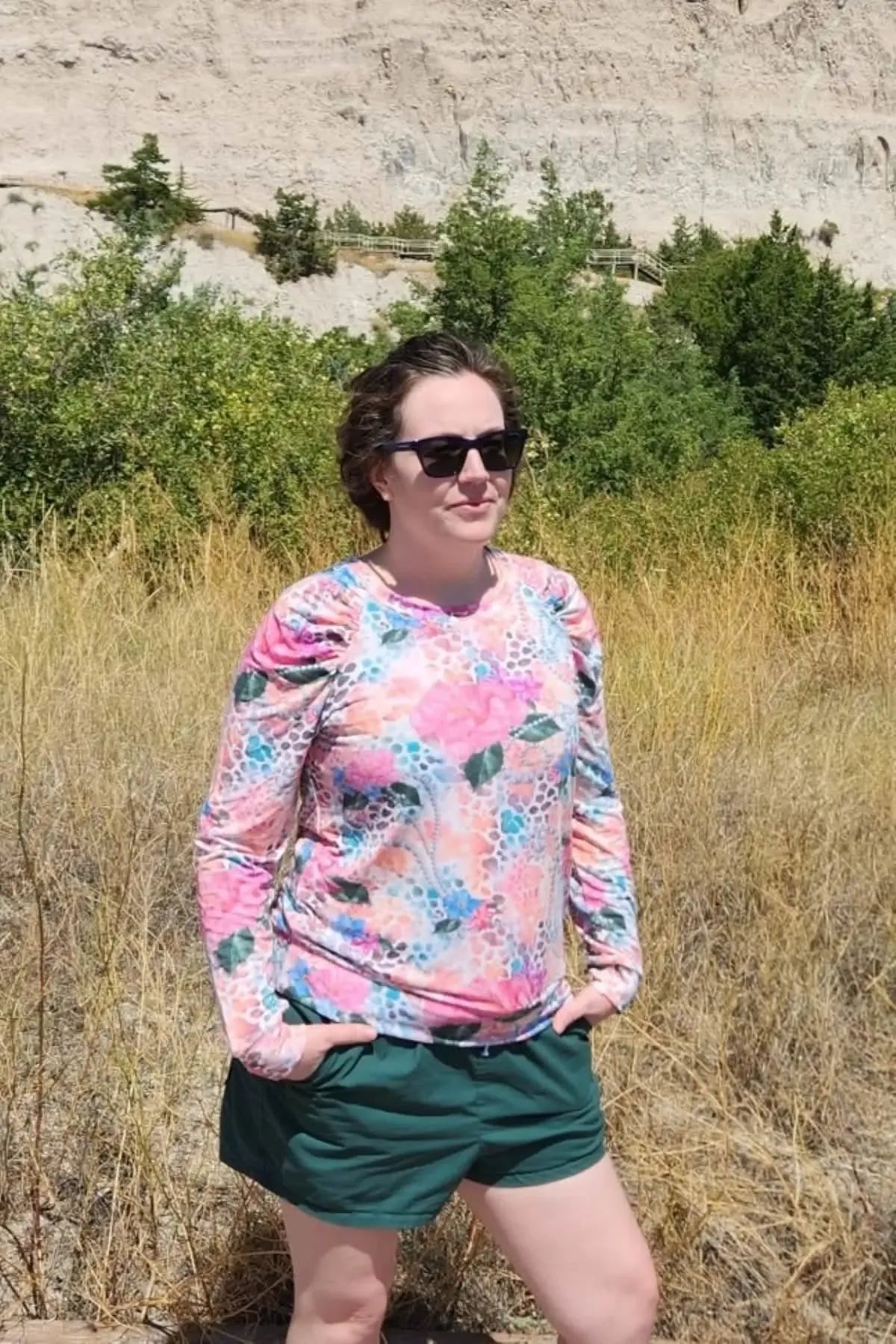 A woman wears a long-sleeved shirt with a vibrant floral and abstract pattern.