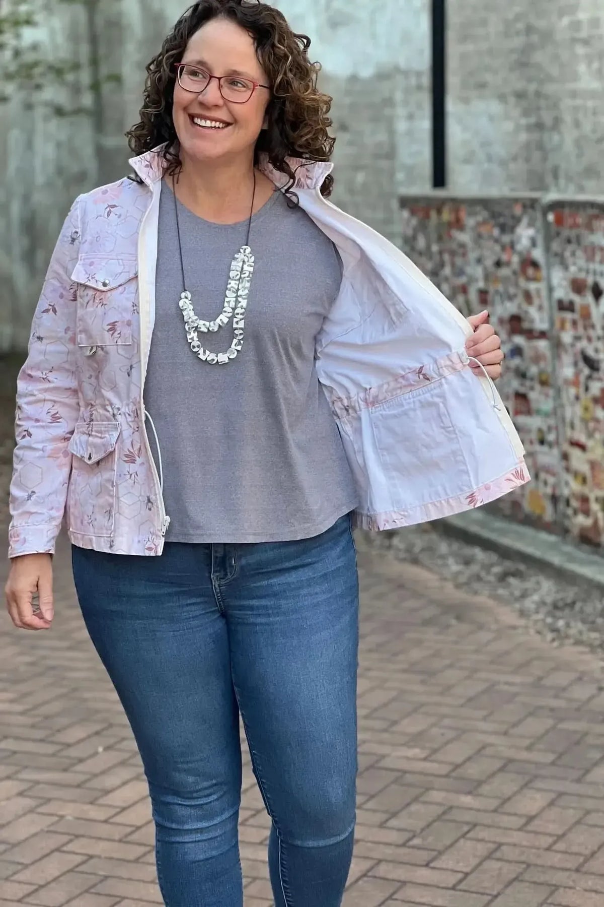 Woman in a peach garden bees print jacket, gray shirt, and blue jeans.