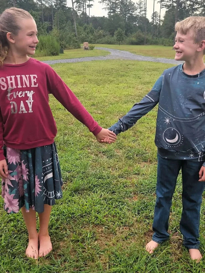 A boy in a celestial print shirt holds hands with a girl in a floral skirt.