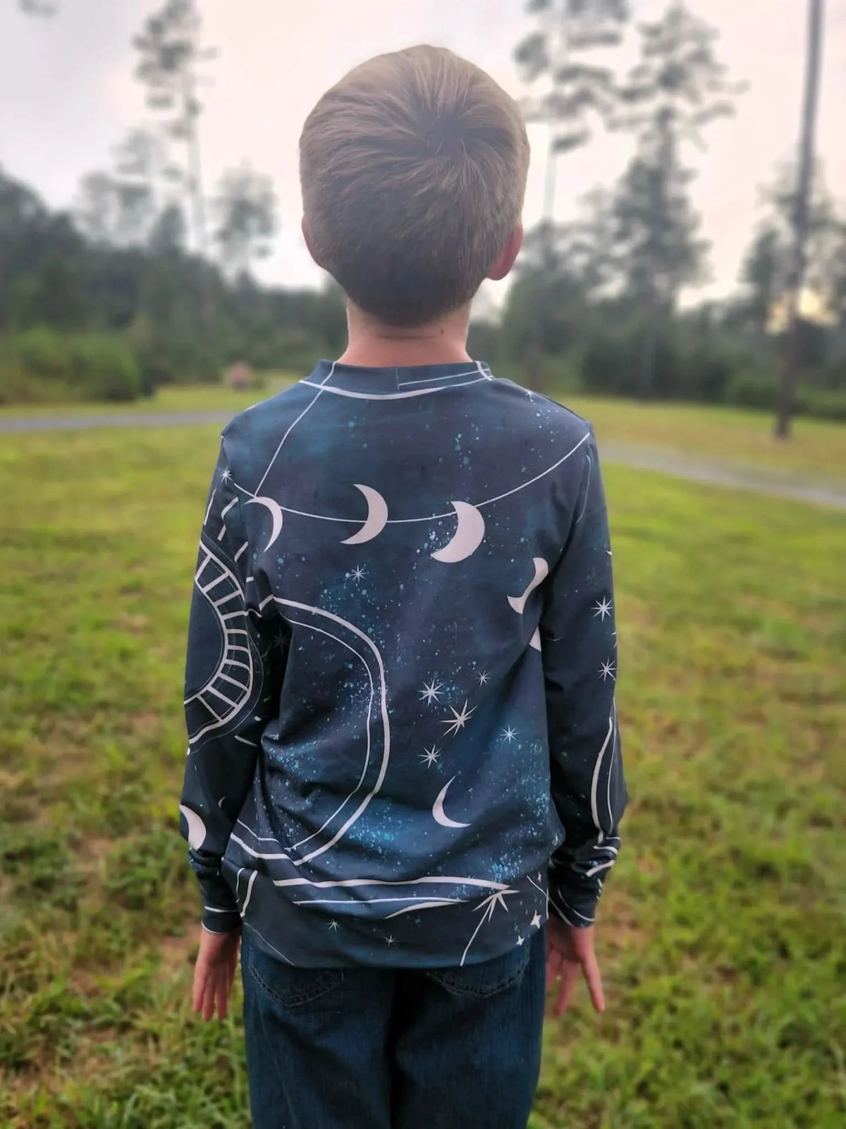 A child from behind wears a long-sleeved shirt with a celestial sky pattern.